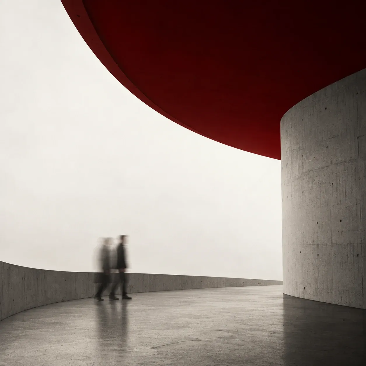 Two blurred figures walking a curved concrete terrace under a deep red canopy, in fog.